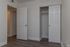 Modern apartment room featuring pristine white walls, sleek dark wood flooring, and a spacious closet with sliding doors.
