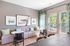 Bright and modern living space featuring a cozy upholstered sofa, elegant marble-top tables, and natural light streaming through large windows with scenic views.