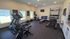 Modern apartment gym featuring state-of-the-art exercise equipment, including treadmill, stationary bike, free weights, and a bench, with natural light enhancing the workout ambiance.