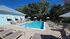 Charming outdoor pool area with luxurious sun loungers and umbrellas, surrounded by lush greenery and a modern blue siding building.