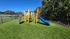 Vibrant playground with colorful slides and climbing structures surrounded by lush greenery and open sky.