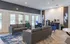 Bright and inviting living room with modern gray sofas, a chic coffee station, and elegant lighting, offering a welcoming ambiance with views of a lush garden through glass doors.