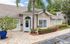 Charming single-story building with inviting landscape, featuring tropical palm trees, vibrant flowers, and a welcoming entrance.