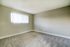 Bright, empty room with freshly carpeted floors and a window with vertical blinds.