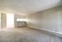 Bright, airy room with open layout and carpeted flooring, leading into a well-lit kitchen area.