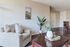 Inviting living room with cozy armchair, elegant coffee table, and vibrant greenery, complemented by chic wall art and warm wooden flooring.