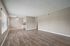 Bright and spacious living room with elegant wood flooring and large windows, featuring a cozy dining area and modern kitchen.