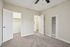 Bright bedroom with soft gray carpeting, featuring an open closet and white doors, perfect for modern living.