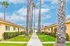 Charming courtyard view with vibrant yellow apartments, lush green lawns, and elegant palm trees under a bright blue sky.