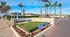 Ocean Air Apartment Homes entrance with palm trees, vibrant landscaping, and welcoming signs under a sunny sky.