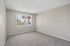 Bright, airy apartment room with plush carpet, neutral walls, and large window featuring serene outdoor views.