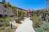 Charming apartment exterior with lush landscaping, inviting pathways, and cozy seating areas under clear blue skies.
