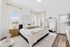 Bright, serene bedroom featuring a luxurious bed, elegant mirror, and soft natural light accents, highlighting modern decor.