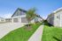 Charming suburban duplex with modern design, featuring a lush green lawn and spacious driveways under a clear blue sky.
