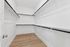 Spacious and elegant walk-in closet with sleek design and ample hanging space, featuring polished wooden flooring and bright white walls.