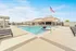 Luxurious apartment complex featuring an inviting pool area with stylish lounge chairs and pergolas, complemented by a striking American flag under a clear blue sky.