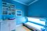Modern tanning room with sleek sunbed and elegant blue decor, complemented by stylish shelving and artistic wall art.