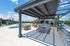 Luxurious outdoor pool area with shaded seating, barbecue grills, and lush greenery under a clear blue sky.