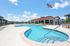 Vibrant apartment complex with inviting swimming pool, sun loungers, and beautiful landscaping under a clear blue sky.