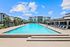 Luxurious apartment complex featuring a sparkling swimming pool with lounge chairs and modern architecture under a bright blue sky.