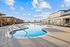Luxurious outdoor pool area with modern lounge chairs and wooden cabanas under a bright blue sky.