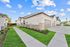 Charming suburban street with modern single-story homes featuring lush green lawns and spacious driveways under a clear blue sky.