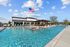 Luxurious apartment complex featuring a sparkling outdoor swimming pool with sun loungers, under a clear blue sky adorned by a waving flag, perfect for relaxation and leisure.
