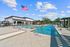 Luxurious pool area featuring lounge chairs, a sparkling blue swimming pool, and a modern clubhouse against a clear blue sky.