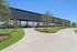 Eight covered and lighted Pickleball courts with sleek black exterior, surrounded by lush landscaped greenery and winding pathways under a clear blue sky.