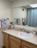 Inviting bathroom with wooden cabinetry, a large mirror, colorful decor, and modern fixtures.