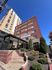 Brick apartment building with a modern entrance and lush greenery under a clear blue sky.