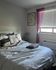 Cozy bedroom with plush bedding, soft natural light filtering through purple curtains, and tasteful wall art.