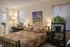 Cozy bedroom with chic decor featuring a patterned bedspread, classic artwork, and lush green plants, creating a warm and inviting ambiance.