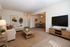 Elegant living room with modern decor, featuring a cozy beige sofa, stylish wooden coffee table, and a wall-mounted TV, leading into an inviting dining area.
