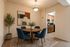 Cozy dining area with a stylish round wooden table, blue chairs, modern art, and a glimpse into a classic kitchen.