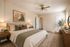 Elegant bedroom with neutral tones, featuring a comfortable bed adorned with stylish pillows, modern artwork, and warm lighting creating a cozy ambiance.