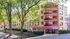Inviting apartment building nestled among lush trees, featuring vibrant red balconies and expansive windows.