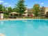 Inviting apartment complex features a sparkling swimming pool with lounge chairs, surrounded by lush greenery and modern buildings.