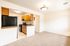 Bright and inviting kitchen with modern appliances and wooden cabinetry, adjacent to a cozy living area with plush carpeting.