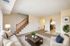 Inviting living room with elegant staircase, cozy beige sofa, and modern decor leading to a spacious kitchen area.