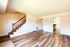 Bright living area with elegant wood flooring, showcasing a contemporary staircase leading to an upper floor, and an inviting doorway to a modern kitchen.