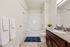 Modern bathroom with elegant white fixtures, cherry wood cabinetry, and plush blue rug, showcasing a serene and inviting space.