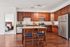 Modern kitchen with rich wooden cabinetry, stainless steel appliances, and an inviting island with seating. Adjacent is an elegantly furnished bedroom, offering a glimpse of comfort and style.