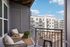 Charming balcony view featuring cozy seating, vibrant greenery, and overlooking modern apartment complex under a bright blue sky.