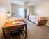 Inviting bedroom featuring two cozy twin beds, a stylish desk with a modern lamp, and natural light streaming through the window for a comfortable, serene atmosphere.