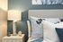 Chic bedroom with modern decor, featuring a stylish gray headboard, patterned pillows, and a bedside lamp.
