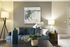 Elegant living room with a modern blue sofa, abstract wall art, decorative cushions, and chic lighting.