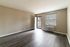 Bright and airy empty living room with wood flooring, large window, and front door access.
