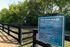 A welcoming entrance to a dog park with a sign displaying dog park rules, surrounded by lush greenery.
