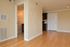 Modern apartment interior featuring a wooden floor, a view of a hallway, and a glimpse of a kitchen area.